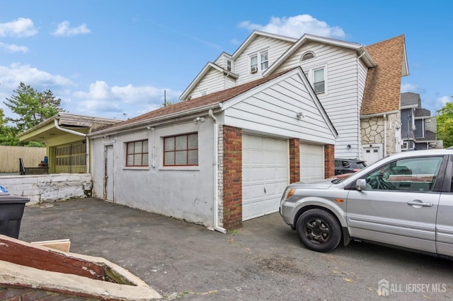 view of side of property with a shingled roof, brick siding, and driveway