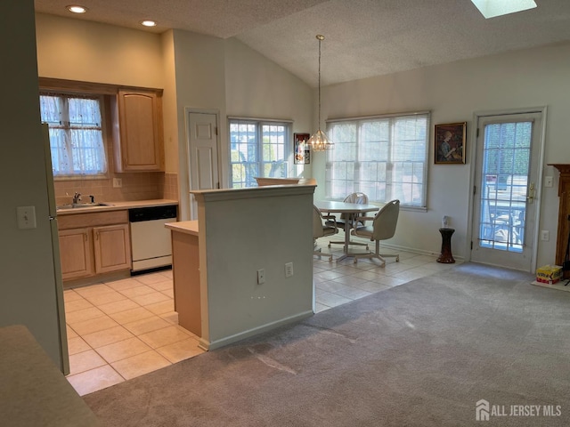 kitchen featuring white dishwasher, hanging light fixtures, light carpet, sink, and lofted ceiling with skylight