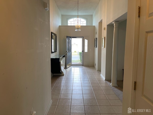 doorway with decorative columns, a high ceiling, a textured ceiling, and light tile patterned floors