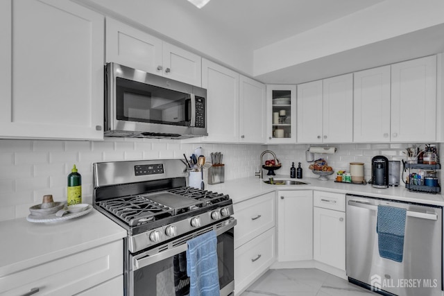 kitchen with stainless steel appliances, a sink, light countertops, white cabinets, and light marble finish floors