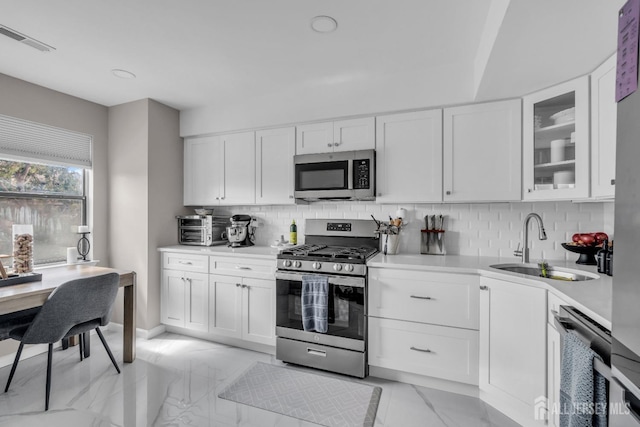 kitchen featuring stainless steel appliances, a sink, light marble finish flooring, and light countertops
