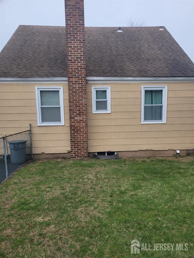 rear view of house with fence, a chimney, a yard, and a shingled roof