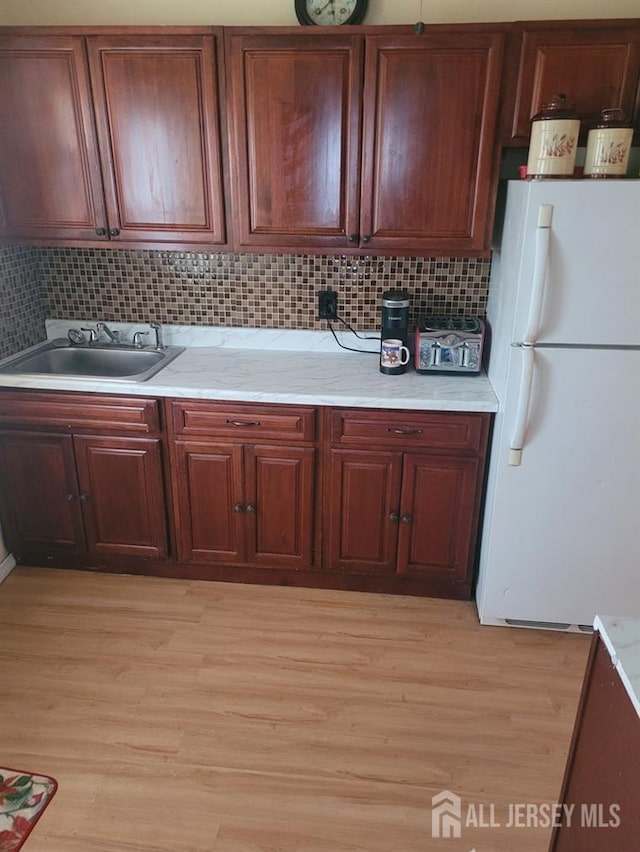 kitchen featuring a sink, light wood-style floors, decorative backsplash, and freestanding refrigerator