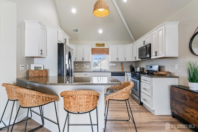 kitchen featuring visible vents, a kitchen breakfast bar, a peninsula, stainless steel appliances, and a sink