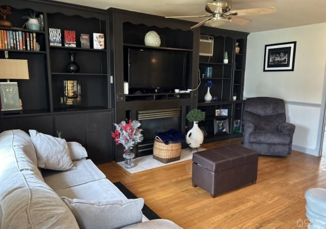 living room featuring built in shelves, ceiling fan, and wood-type flooring