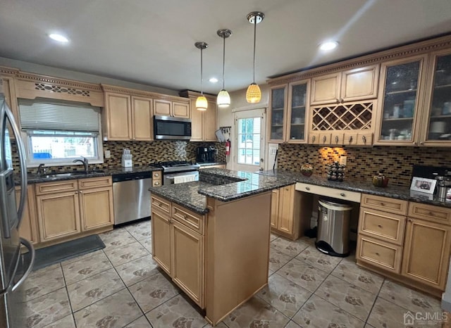 kitchen with sink, decorative light fixtures, appliances with stainless steel finishes, a kitchen island, and dark stone counters