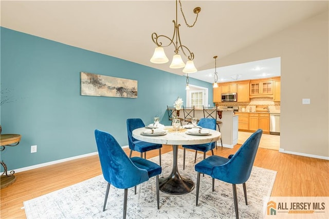 dining room with light wood-type flooring, baseboards, and vaulted ceiling
