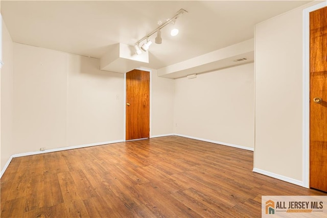 spare room with wood finished floors, baseboards, and rail lighting