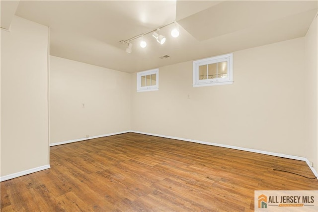 finished below grade area featuring track lighting, baseboards, and wood finished floors