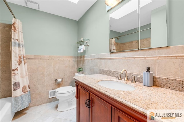 full bath featuring tile walls, tile patterned flooring, toilet, vanity, and a skylight