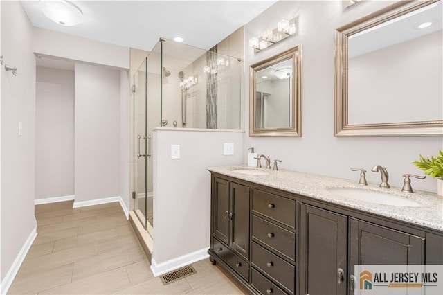 bathroom featuring a stall shower, double vanity, and baseboards