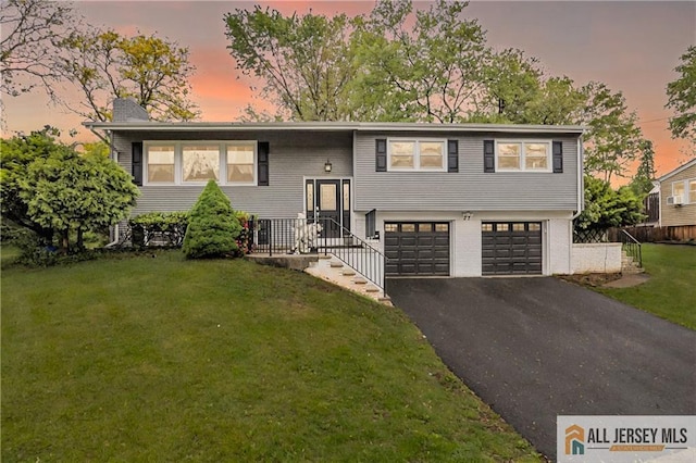 bi-level home featuring an attached garage, asphalt driveway, a front lawn, and a chimney