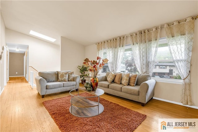 living area featuring light wood-type flooring, baseboards, vaulted ceiling, and a skylight