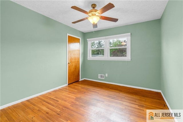 empty room featuring wood finished floors, baseboards, a ceiling fan, and a textured ceiling
