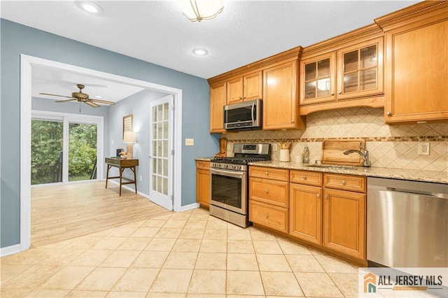 kitchen featuring appliances with stainless steel finishes, a sink, decorative backsplash, light stone countertops, and recessed lighting