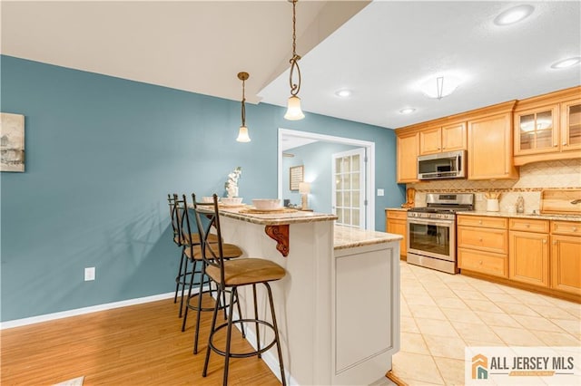 kitchen featuring appliances with stainless steel finishes, a breakfast bar, decorative backsplash, glass insert cabinets, and pendant lighting