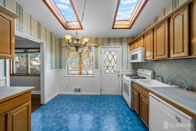 kitchen with a skylight, white appliances, a sink, and tile countertops