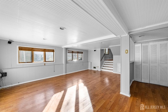 unfurnished living room with stairway, wood finished floors, and beamed ceiling