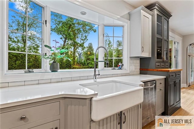 kitchen with stainless steel dishwasher, a sink, glass insert cabinets, light wood-style floors, and decorative backsplash