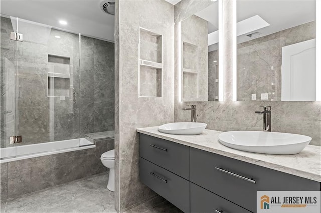 full bathroom featuring toilet, tile walls, double vanity, combined bath / shower with glass door, and marble finish floors