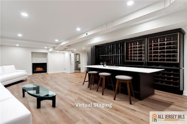 wine room featuring wood finished floors, recessed lighting, baseboards, bar area, and a lit fireplace
