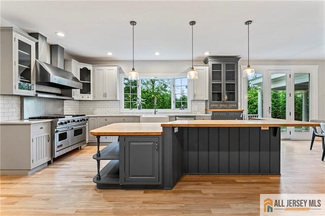 kitchen with appliances with stainless steel finishes, wall chimney exhaust hood, butcher block counters, a breakfast bar area, and decorative backsplash