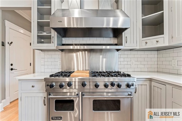 kitchen featuring wall chimney exhaust hood, double oven range, light countertops, glass insert cabinets, and crown molding