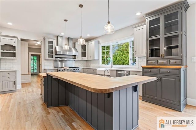 kitchen featuring wood counters, wall chimney range hood, tasteful backsplash, healthy amount of natural light, and recessed lighting