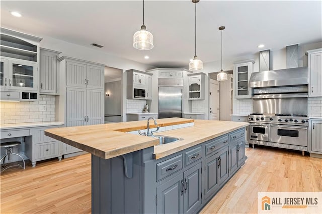 kitchen with premium appliances, wall chimney exhaust hood, a sink, wooden counters, and backsplash