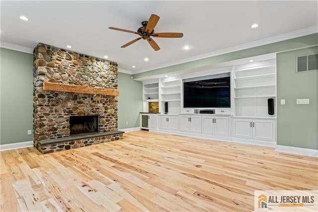 unfurnished living room with ornamental molding, light wood-type flooring, ceiling fan, a stone fireplace, and baseboards