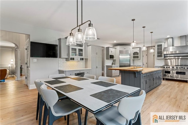 dining space featuring arched walkways, ornate columns, light wood-type flooring, baseboards, and recessed lighting