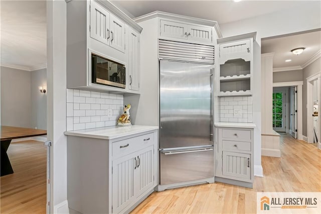 kitchen with stainless steel built in fridge, ornamental molding, backsplash, light wood-type flooring, and light countertops