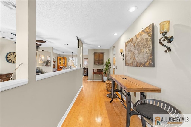 corridor featuring a textured ceiling, recessed lighting, arched walkways, light wood finished floors, and baseboards