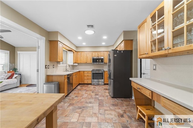 kitchen with visible vents, a sink, appliances with stainless steel finishes, light countertops, and glass insert cabinets