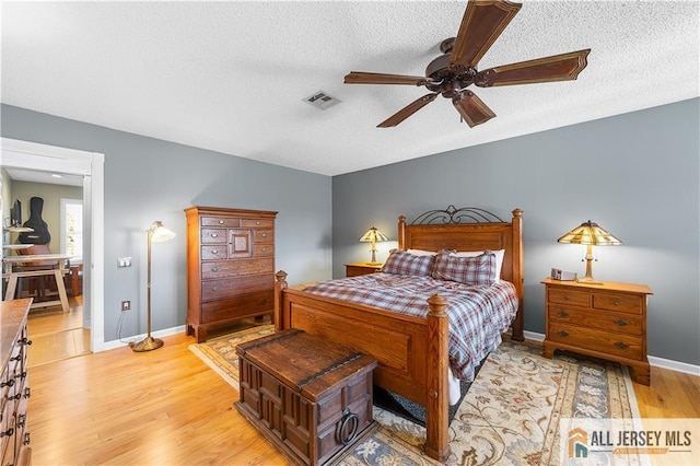 bedroom featuring visible vents, a textured ceiling, light wood finished floors, baseboards, and ceiling fan