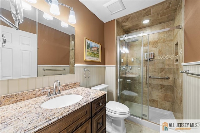 full bathroom with visible vents, a wainscoted wall, toilet, a stall shower, and vanity