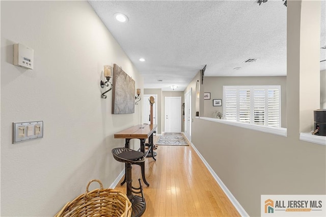 hallway featuring light wood-type flooring, visible vents, baseboards, and a textured ceiling