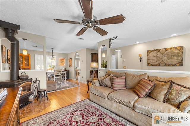 living area with visible vents, a wood stove, wood finished floors, arched walkways, and a ceiling fan