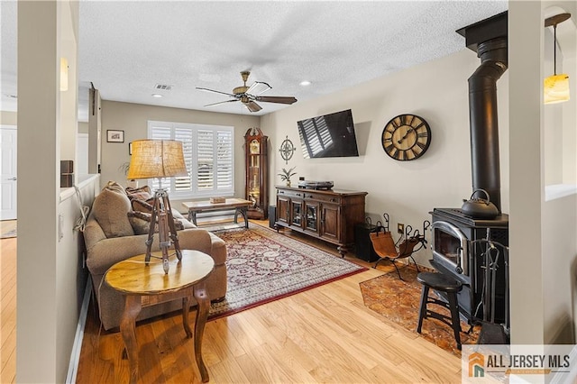 living area featuring a ceiling fan, wood finished floors, visible vents, a wood stove, and a textured ceiling