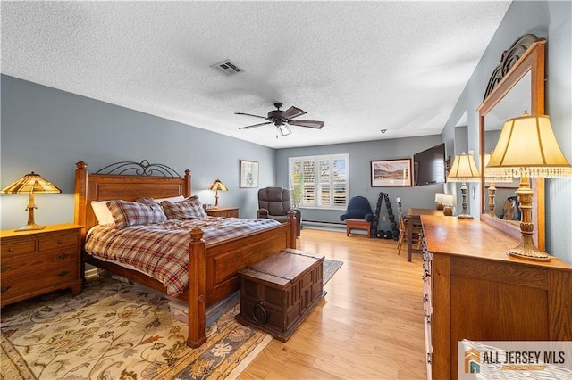 bedroom featuring a textured ceiling, visible vents, a baseboard heating unit, and light wood-type flooring