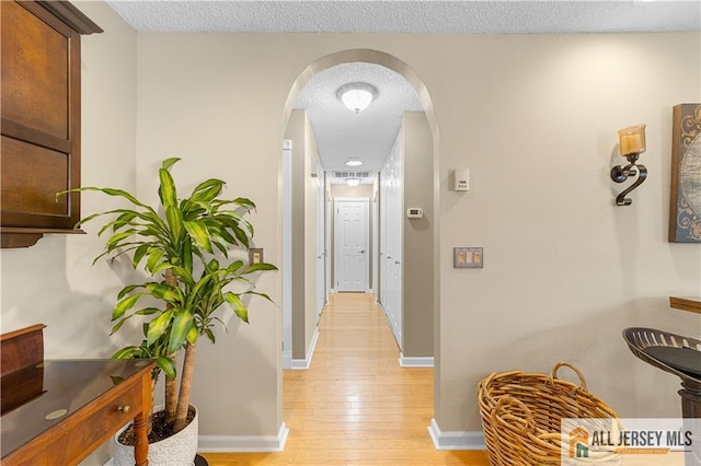 hallway with baseboards, arched walkways, light wood finished floors, and a textured ceiling