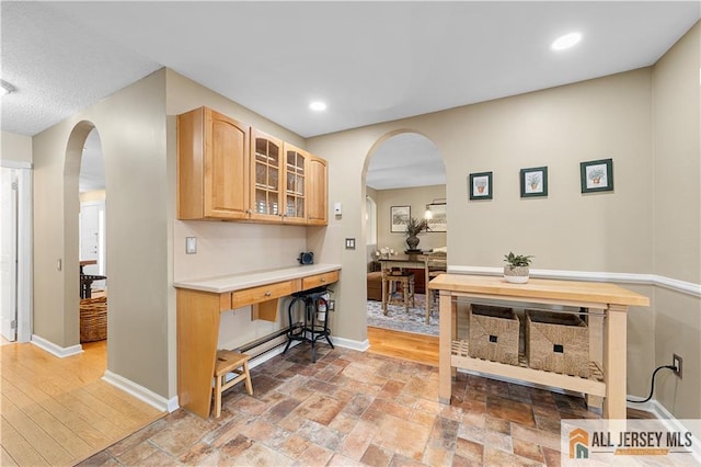 interior space with light brown cabinets, arched walkways, light countertops, glass insert cabinets, and baseboards