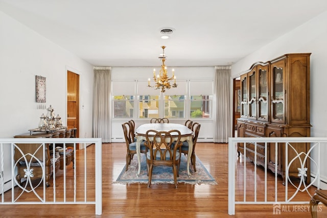 dining area featuring visible vents, wood finished floors, an inviting chandelier, and a baseboard radiator