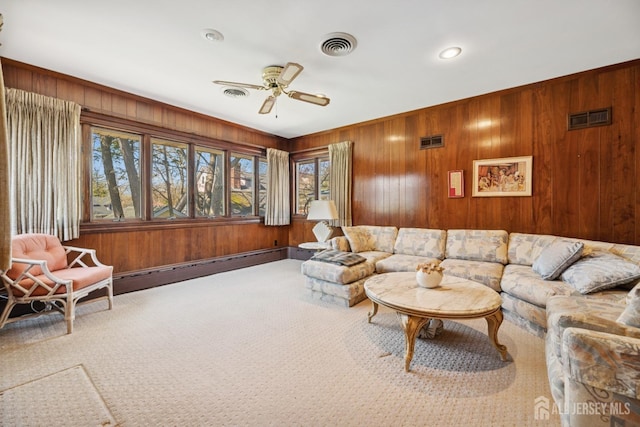 carpeted living area featuring wood walls, visible vents, and a ceiling fan