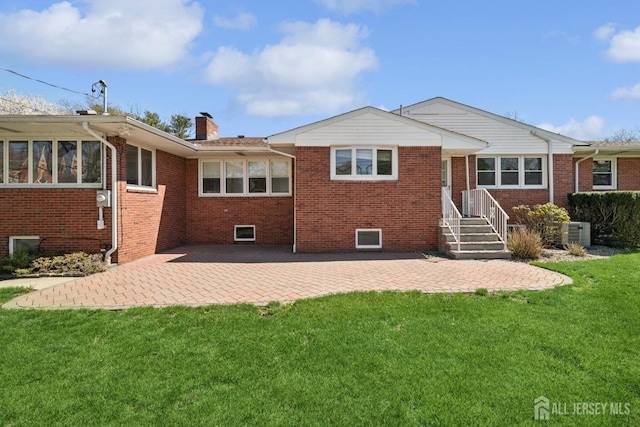 rear view of property with a chimney, a yard, brick siding, a patio, and central AC unit