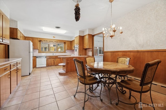 dining space featuring light tile patterned flooring, a wainscoted wall, an inviting chandelier, and wallpapered walls