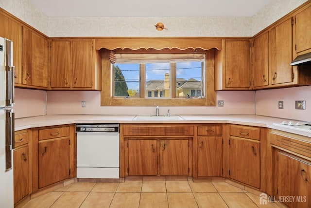 kitchen featuring light countertops, a sink, brown cabinets, and white appliances
