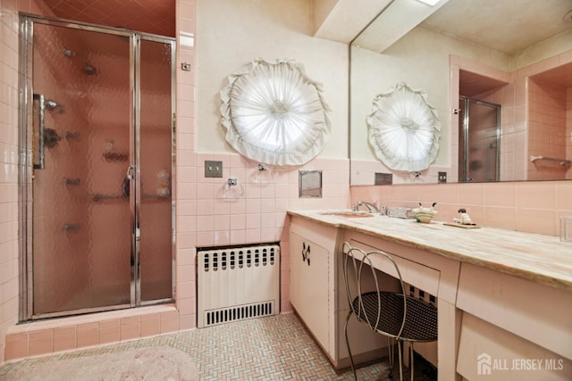bathroom featuring radiator heating unit, vanity, a shower stall, and tile walls