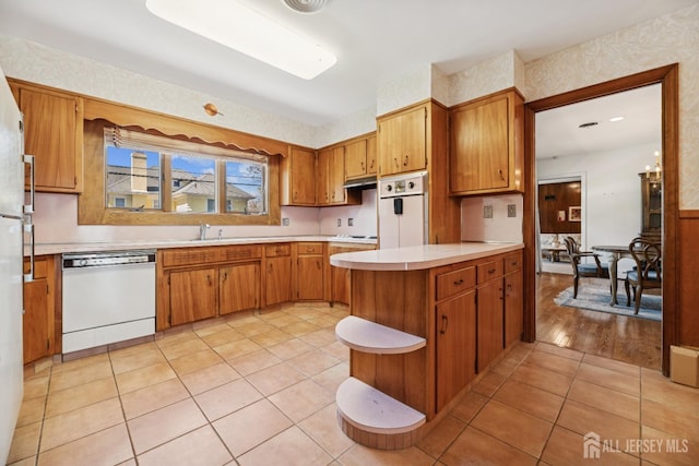 kitchen with brown cabinetry, wall oven, light countertops, and white dishwasher