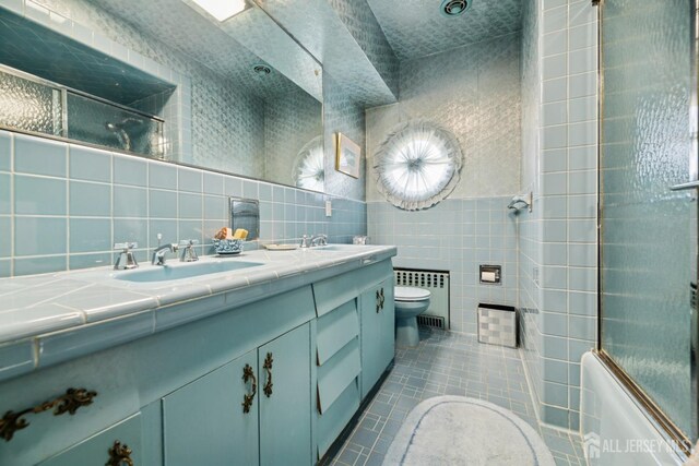 bathroom with radiator, tile walls, a sink, tile patterned floors, and toilet
